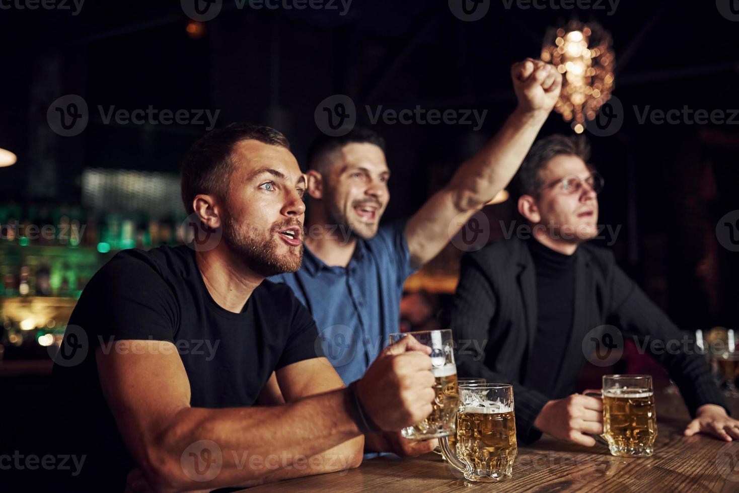 célébrant la victoire. trois fans de sport dans un bar regardent le football. avec de la bière dans les mains photo