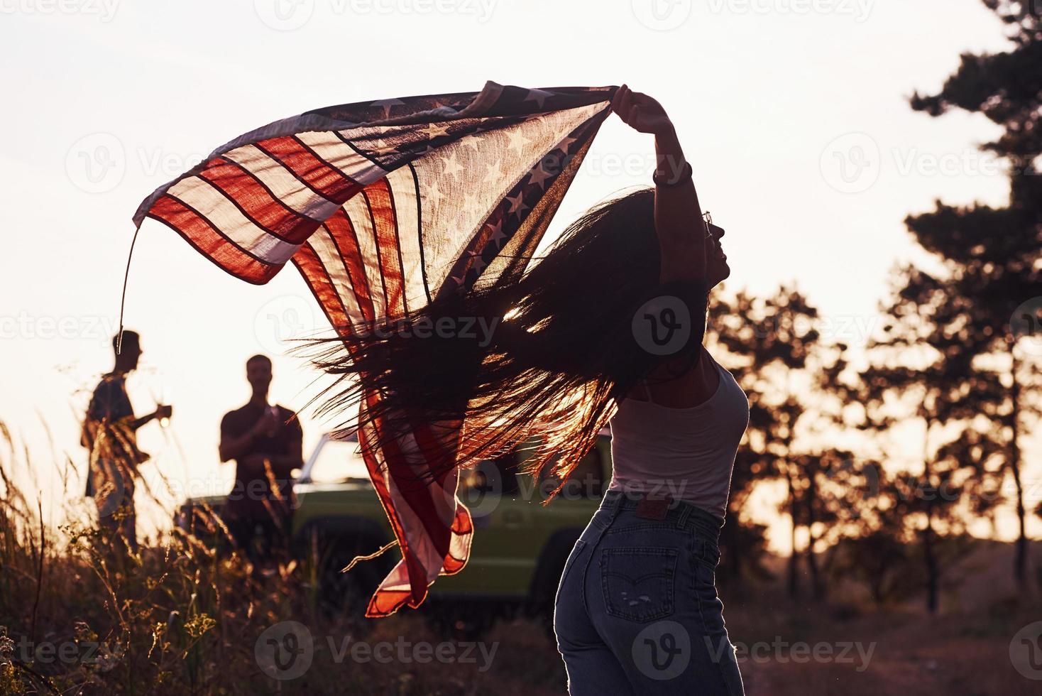 sent la liberté. les amis passent un bon week-end à l'extérieur près de leur voiture verte avec le drapeau américain photo