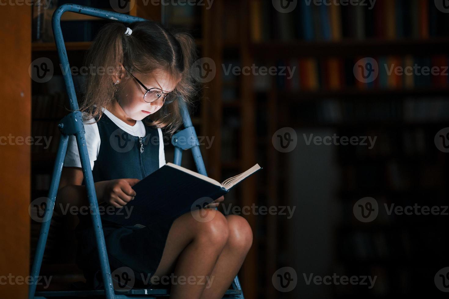 concentration sur la lecture. écolière sur l'échelle dans la bibliothèque pleine de livres. conception de l'éducation photo