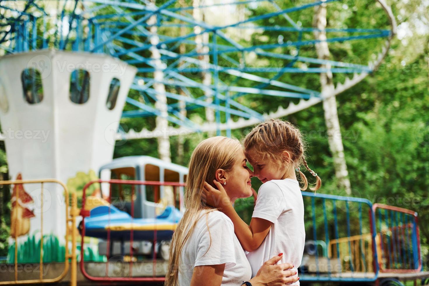 s'aimer. joyeuse petite fille sa mère passe un bon moment dans le parc ensemble près des attractions photo