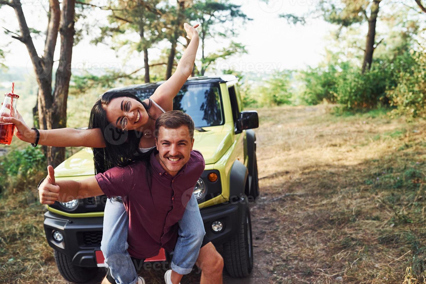 sourire et s'amuser. couple de jeunes alcoolisés s'amusent dans la forêt. jeep verte derrière photo