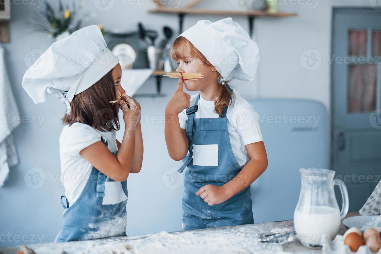 s'amuser avec des spaghettis. enfants de la famille en uniforme de chef blanc préparant la nourriture dans la cuisine photo