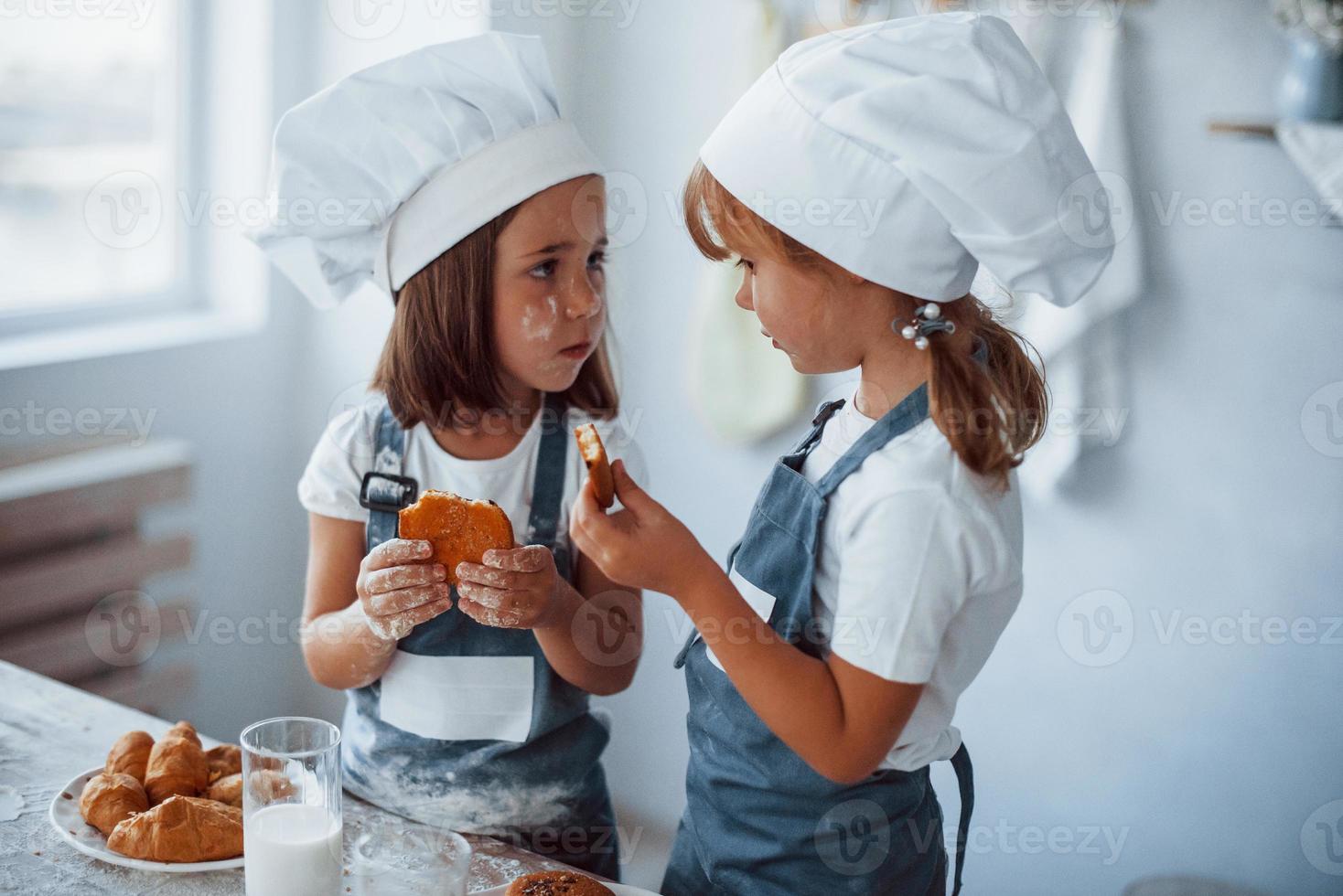 les enfants de la famille en uniforme de chef blanc mangent de la nourriture dans la cuisine photo