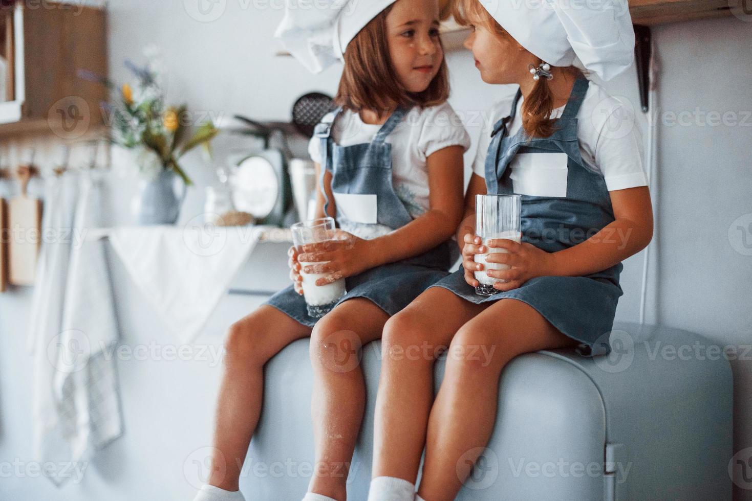 assis sur le frigo. les enfants de la famille en uniforme de chef blanc mangent de la nourriture dans la cuisine photo