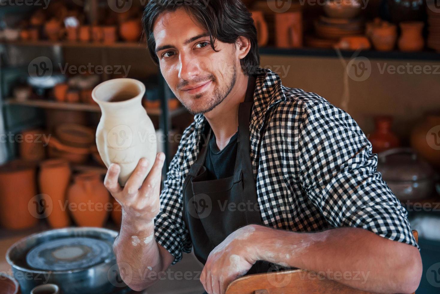 le jeune céramiste tient un pot fait main frais à la main. satisfait des résultats de son travail photo