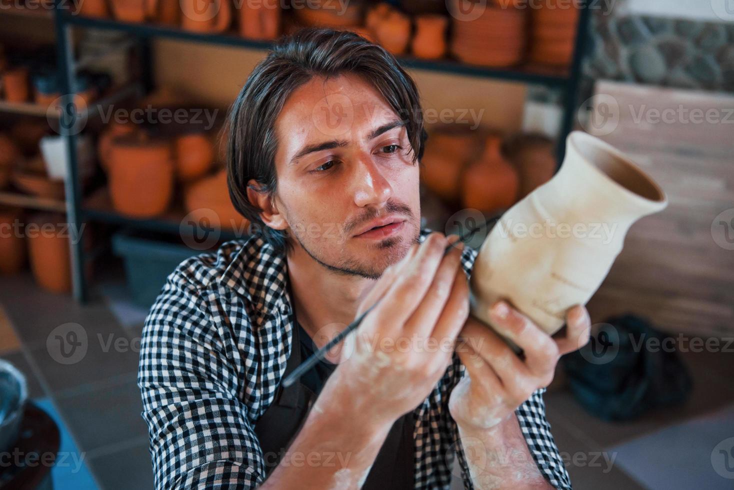 le jeune céramiste tient son pot frais fait à la main et fait quelques détails avec un bâton d'outil spécial photo