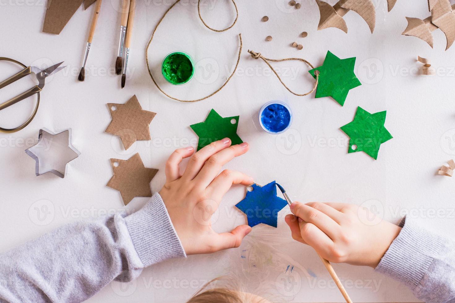 un enfant peint une étoile à la gouache à partir de carton pour des décorations de noël faites à la main. vue de dessus. photo