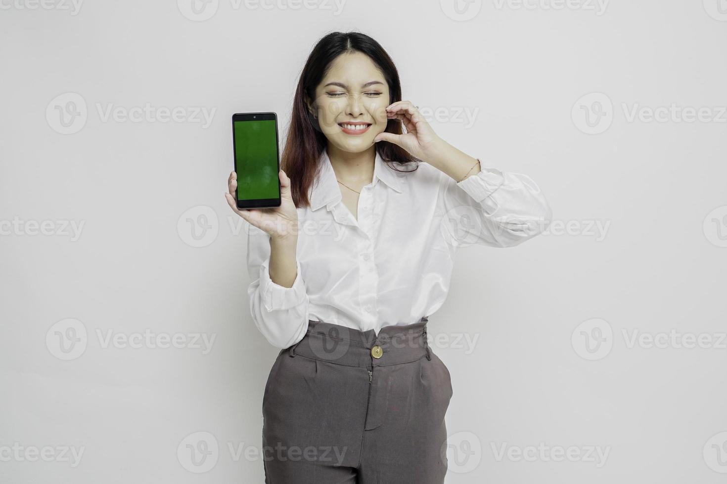 une jeune femme asiatique heureuse portant une chemise blanche, montrant des formes le geste du coeur exprime des sentiments tendres tout en montrant l'espace de copie sur son téléphone photo