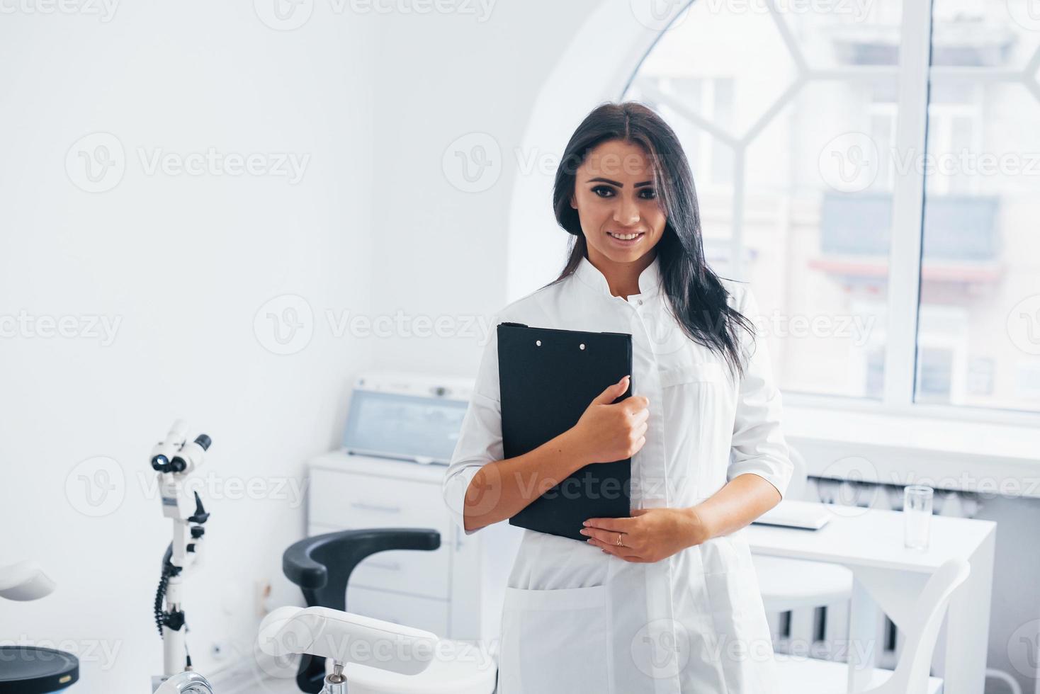 avec bloc-notes dans les mains. femme médecin brune se tient dans un bureau moderne et regarde la caméra photo