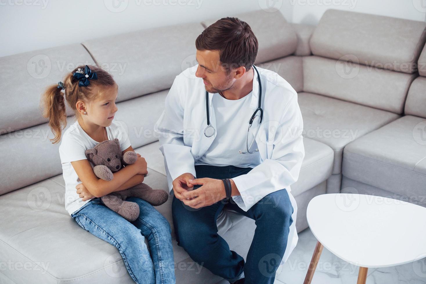 médecin de sexe masculin en uniforme blanc est assis dans la clinique avec une petite fille photo