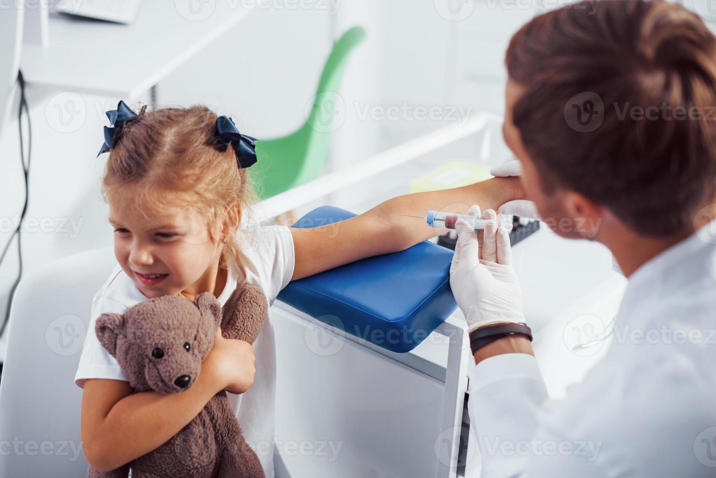 prise de sang. petite fille avec son ours en peluche est à la clinique avec un médecin photo