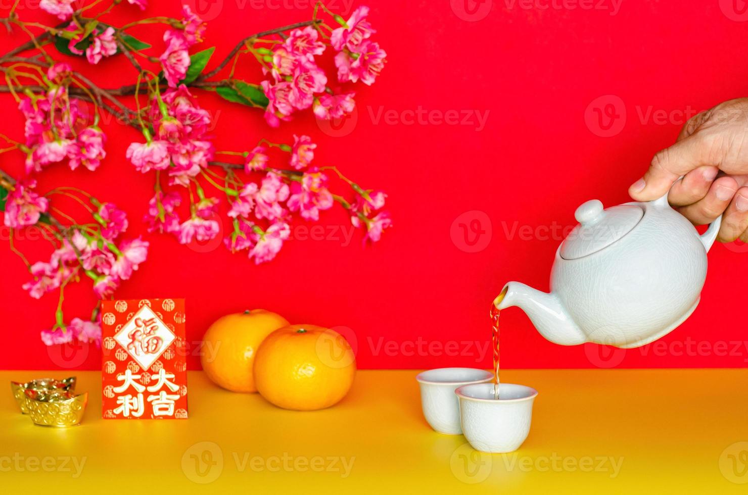 verser à la main le thé du pot pour le concept du nouvel an chinois avec des oranges, une enveloppe rouge ou un mot ang bao signifie une grande fortune et des lingots sur fond de papier pailleté jaune et rouge. photo