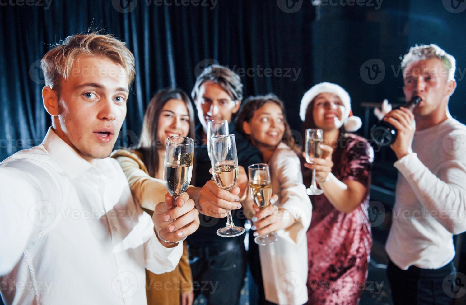 prend un selfie. groupe d'amis joyeux célébrant le nouvel an à l'intérieur avec des boissons dans les mains photo