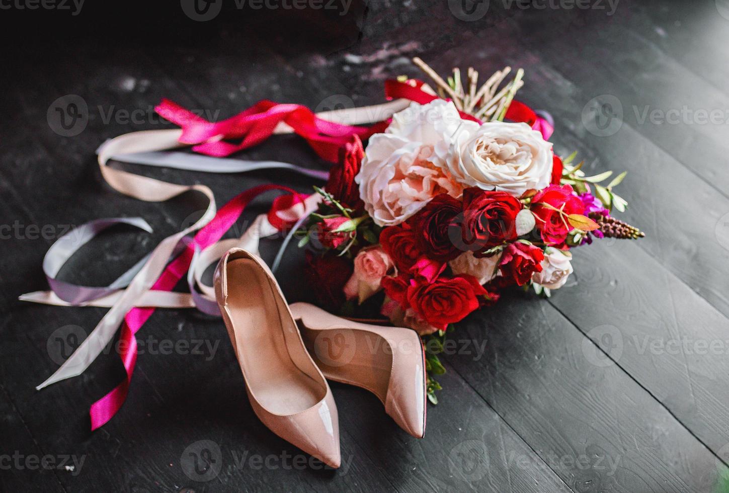 chaussures beiges et bouquet de roses rouges d'une mariée sur un sol en bois noir. compositions de mariage. photo
