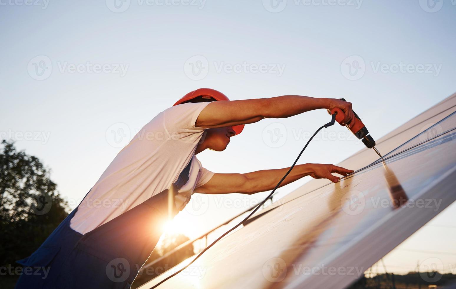 à l'aide d'un tournevis sans fil. travailleur masculin en uniforme bleu à l'extérieur avec des batteries solaires à la journée ensoleillée photo