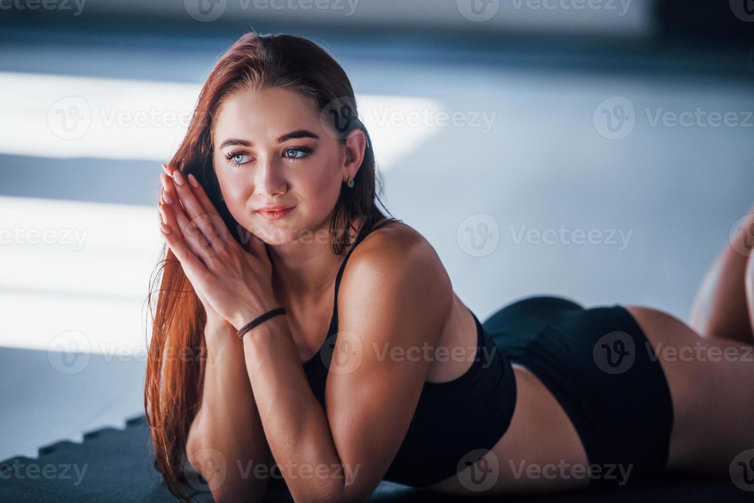 jeune femme au corps mince et en vêtements sportifs noirs allongée sur le tapis de fitness photo