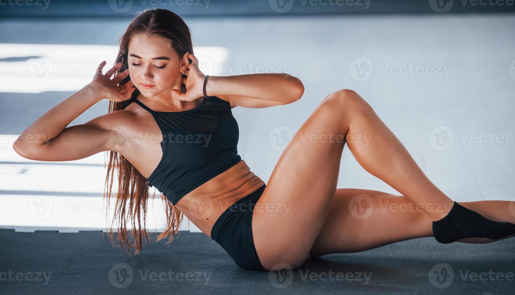 faire des abdos. jeune femme de remise en forme avec un type de corps mince et en vêtements sportifs noirs est dans la salle de gym photo