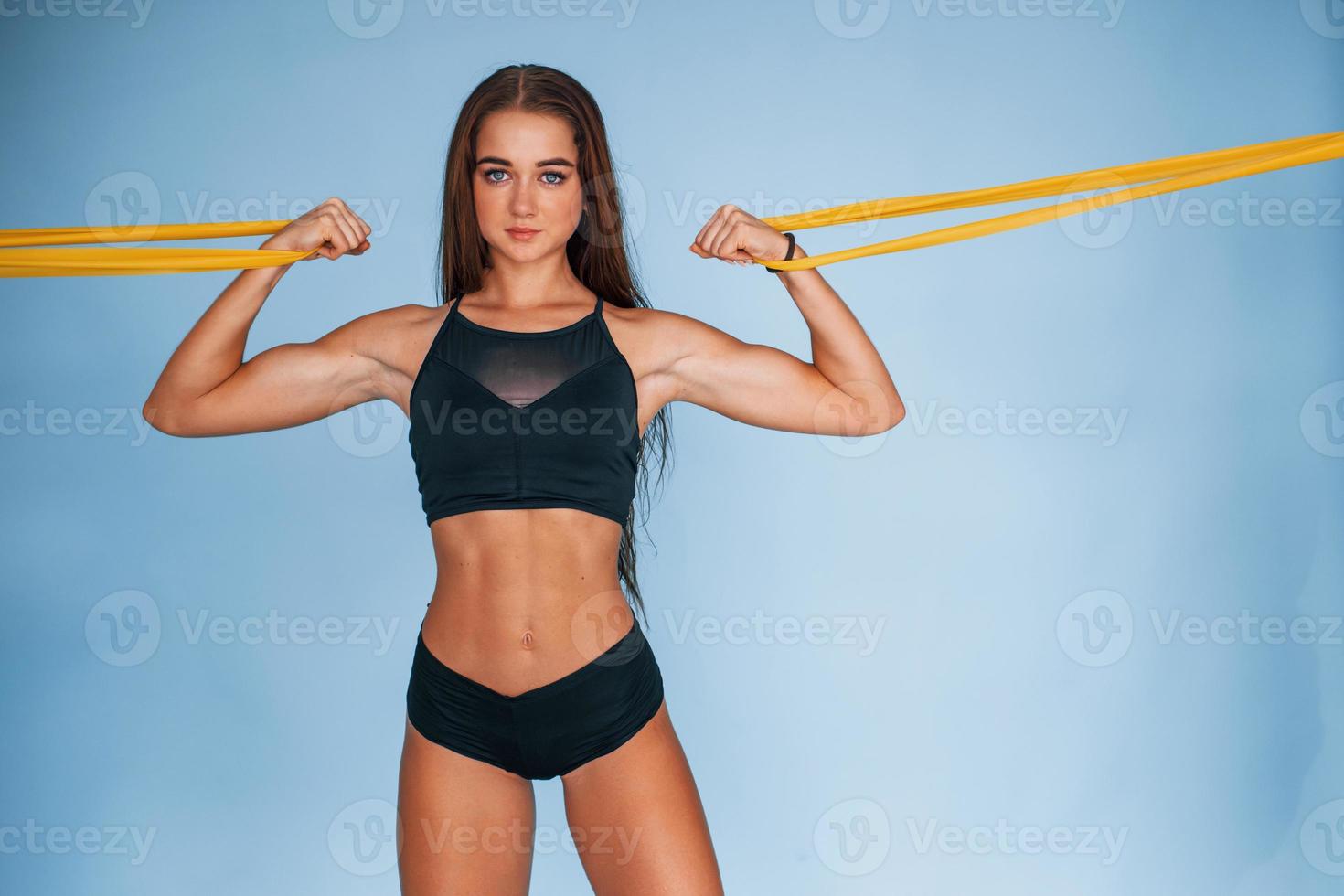 exercice des mains en utilisant une bande de résistance. jeune femme avec un type de corps mince isolé sur fond bleu photo