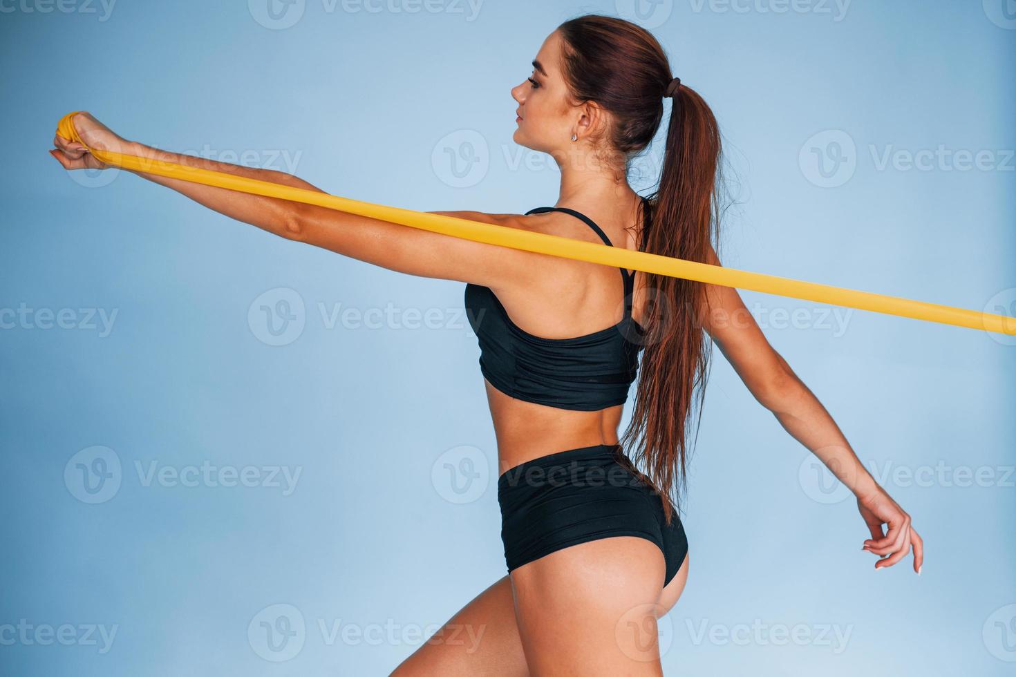 exercice des mains en utilisant une bande de résistance. jeune femme avec un type de corps mince isolé sur fond bleu photo