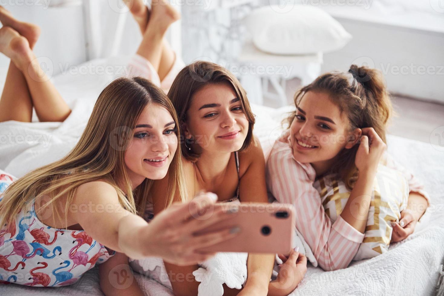 faire selfie en utilisant un téléphone rose. heureuses amies s'amusant à la soirée pyjama dans la chambre photo