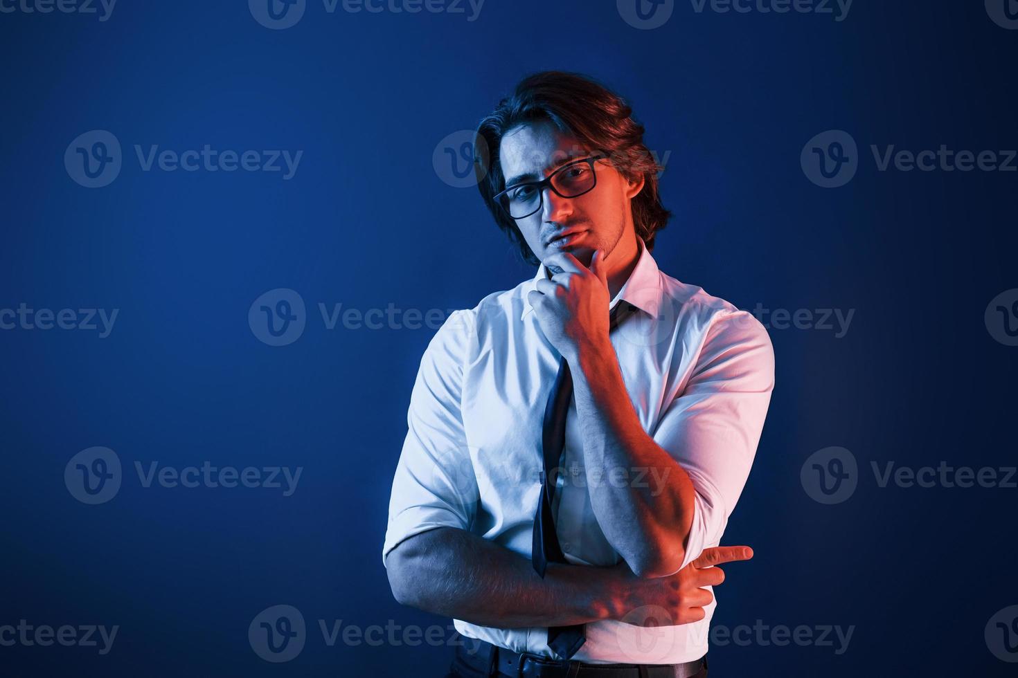 bel homme en tenue de soirée et à lunettes est en studio avec un éclairage au néon bleu photo