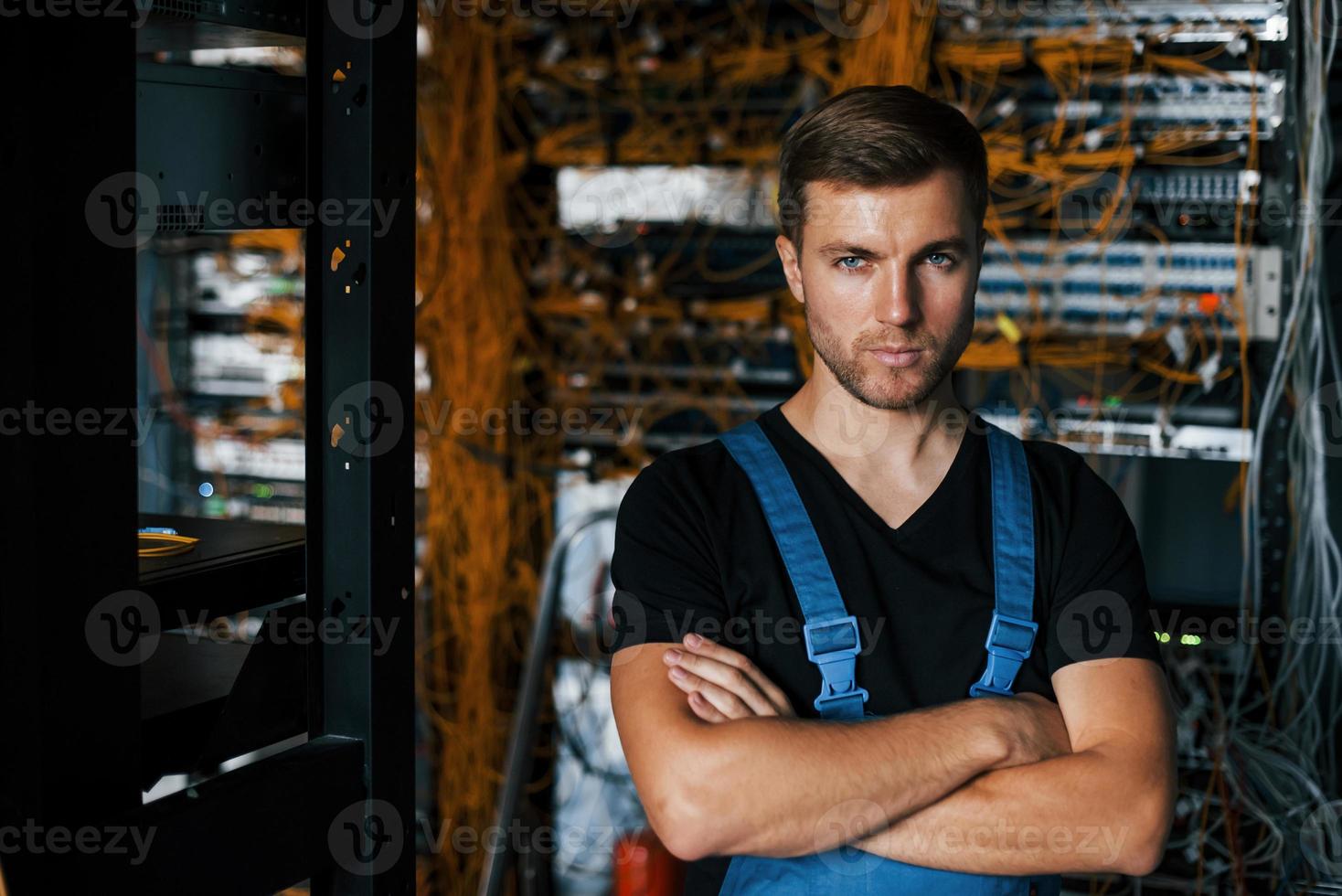 jeune homme en uniforme se dresse contre l'équipement internet dans la salle des serveurs photo