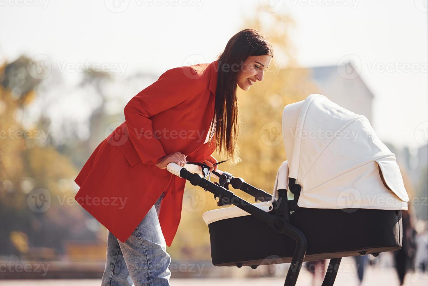 mère en manteau rouge se promener avec son enfant dans le landau dans le parc à l'automne photo