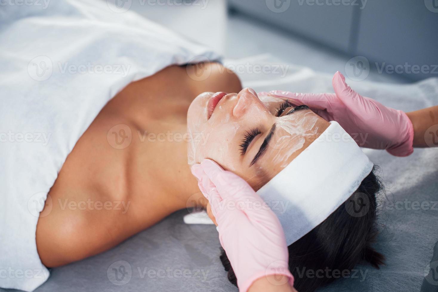 vue rapprochée d'une femme allongée dans un salon de spa et ayant une procédure de nettoyage du visage par le masque photo