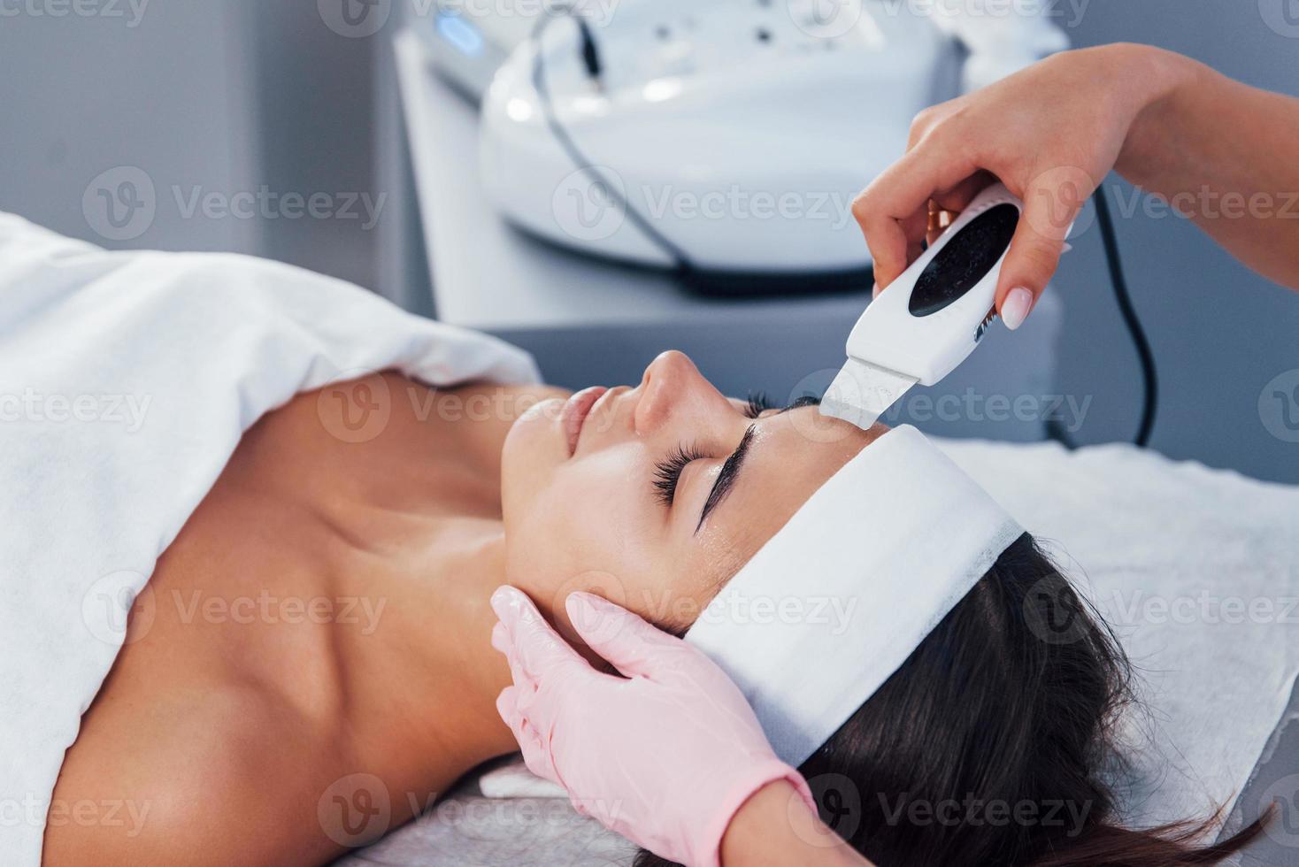 à l'aide d'un appareil spécial. vue rapprochée d'une femme allongée dans un salon de spa et ayant une procédure de nettoyage du visage photo