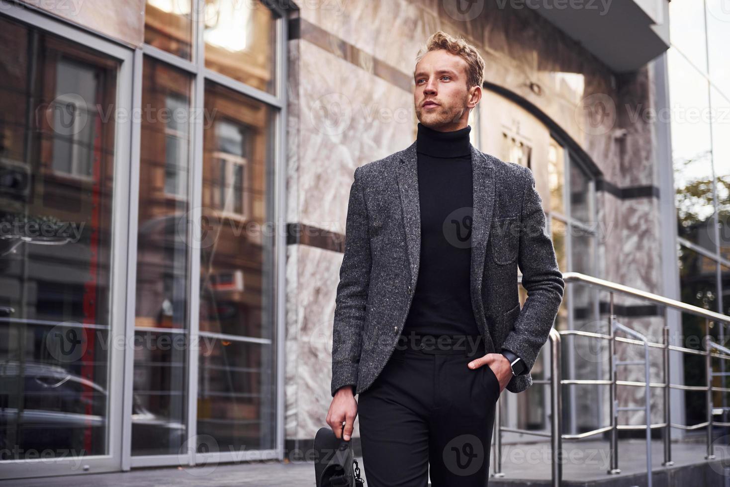 homme en tenue de soirée élégante et avec sac est à l'extérieur contre un bâtiment moderne photo