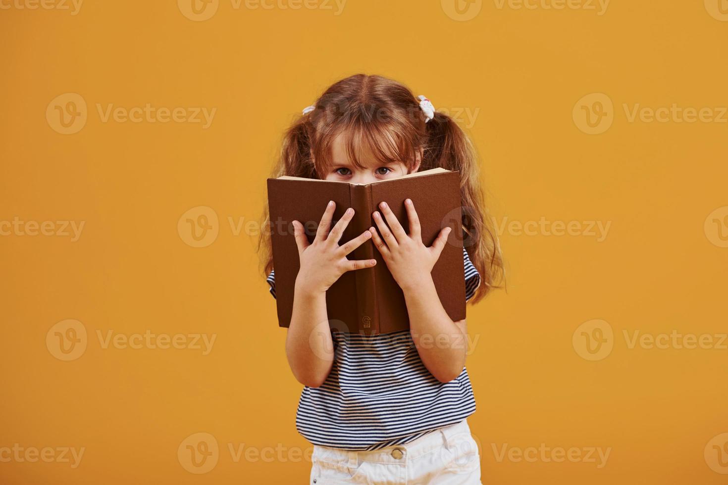 jolie petite fille avec un livre dans les mains en studio sur fond jaune photo