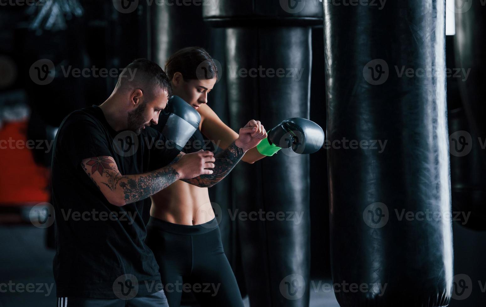 jeune entraîneur de boxe tatoué enseigne à une jeune femme dans la salle de sport photo