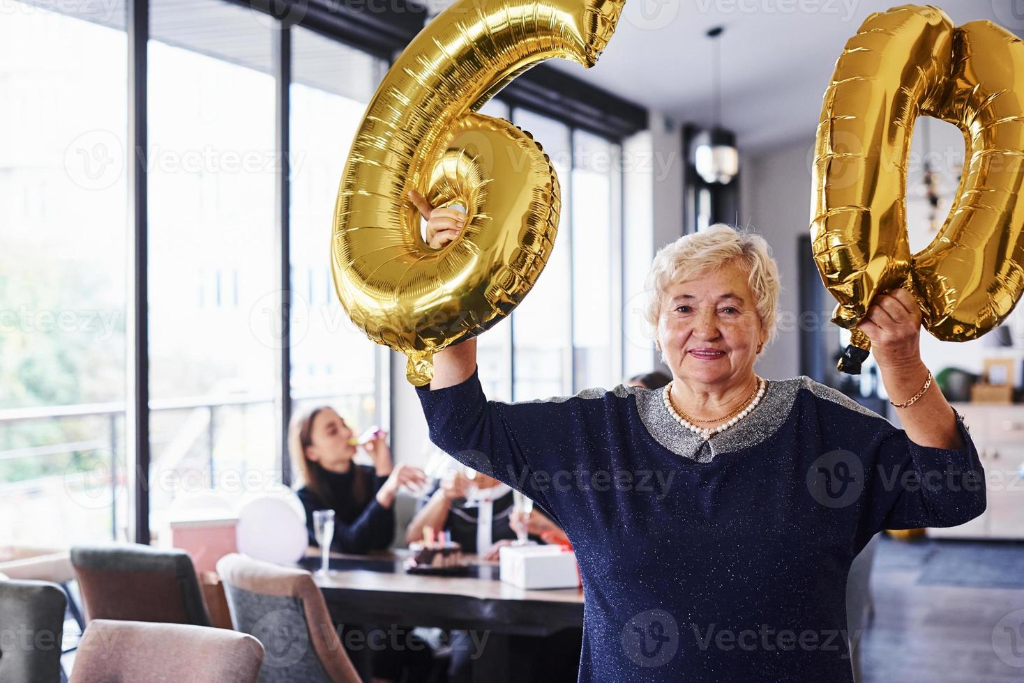 avec des ballons du numéro 60 dans les mains. femme âgée avec famille et amis célébrant un anniversaire à l'intérieur photo