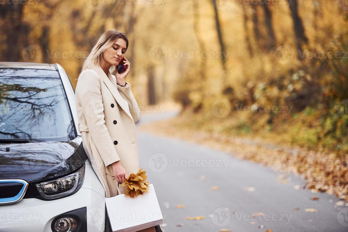 la fille a un appel quand elle se tient près de la voiture. automobile neuve et moderne dans la forêt photo