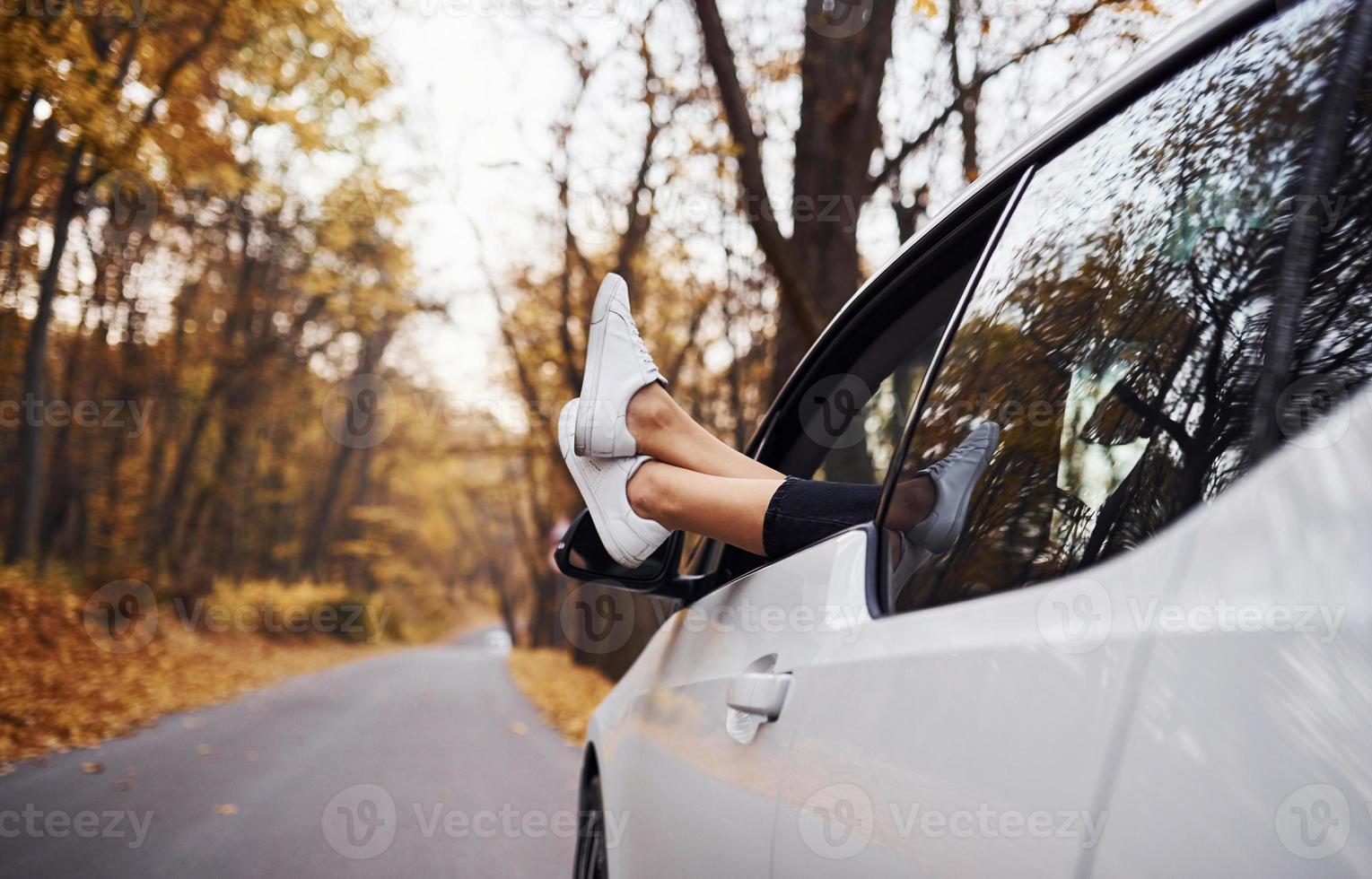 les jambes de la femme sont hors de la fenêtre de la voiture. automobile neuve et moderne dans la forêt photo