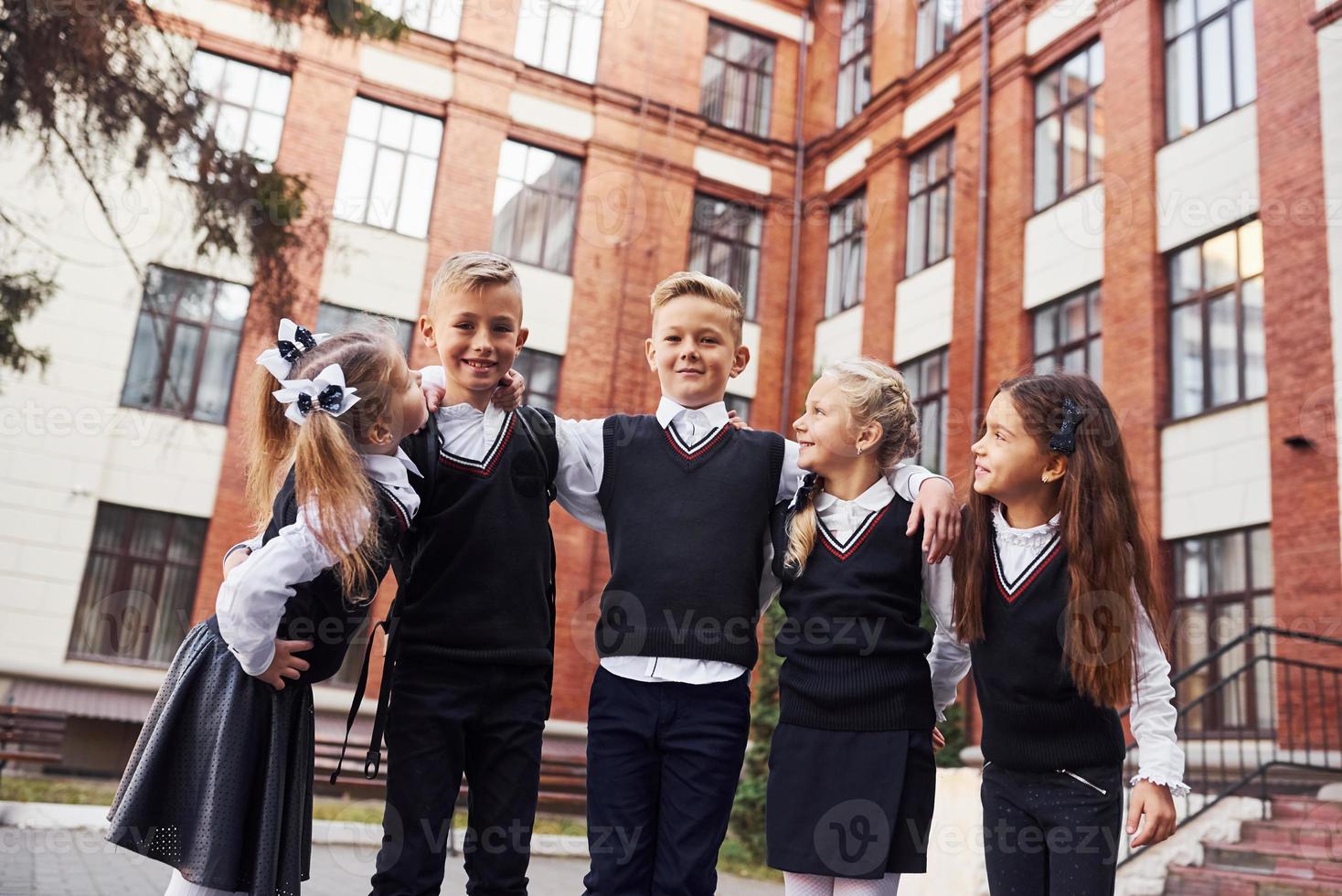 s'amuser et s'embrasser. groupe d'enfants en uniforme scolaire qui est à l'extérieur ensemble près du bâtiment de l'éducation photo