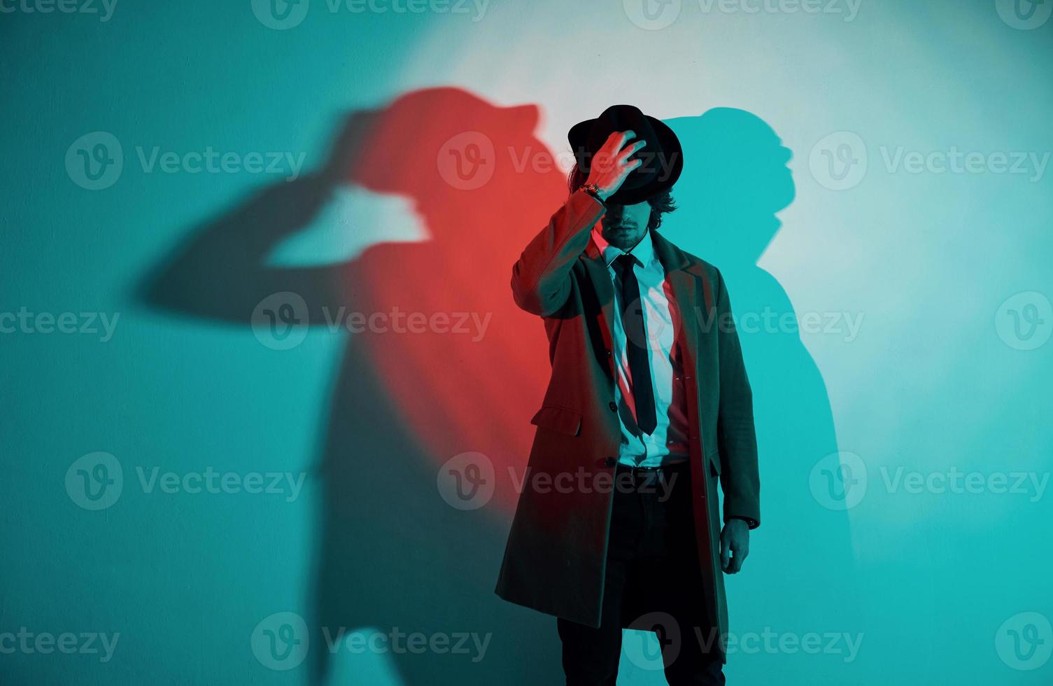 portrait de jeune homme élégant en chapeau, costume et cravate qui se tient dans les néons du studio photo