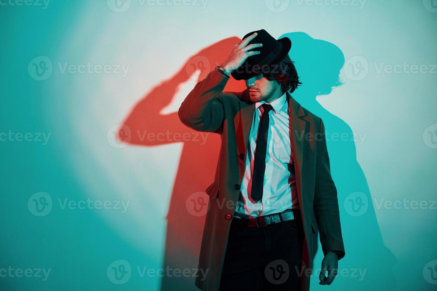 portrait de jeune homme élégant en chapeau, costume et cravate qui se tient dans les néons du studio photo