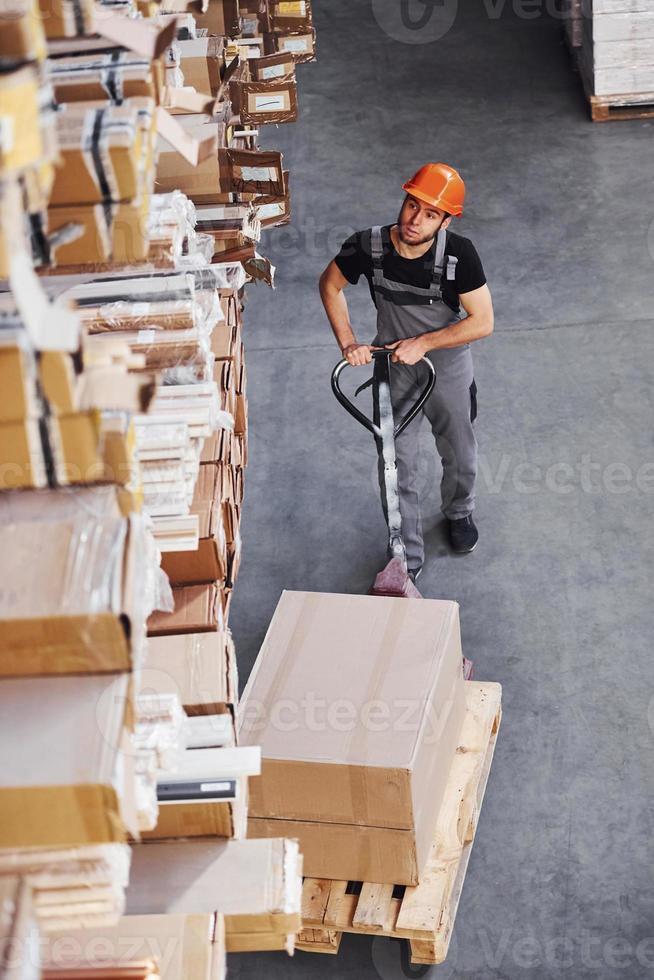 vue de dessus d'un jeune travailleur masculin en uniforme qui se trouve dans l'entrepôt en poussant un transpalette photo