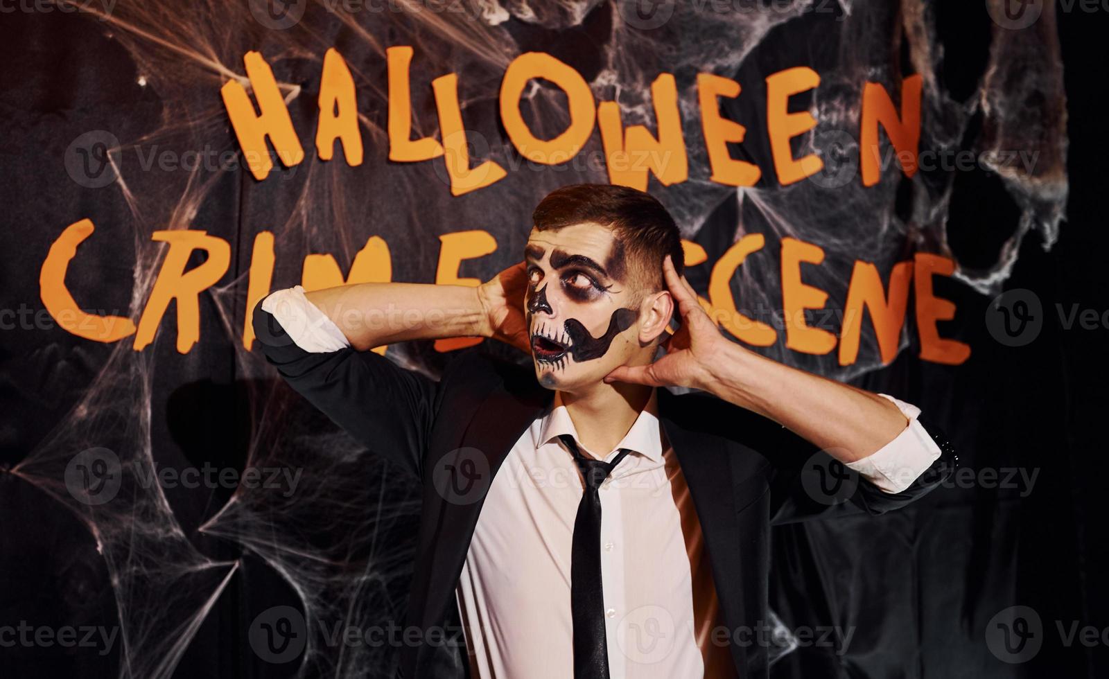 portrait d'homme qui est à la fête d'halloween thématique en maquillage squelette effrayant et costume contre le mur de la scène du crime photo