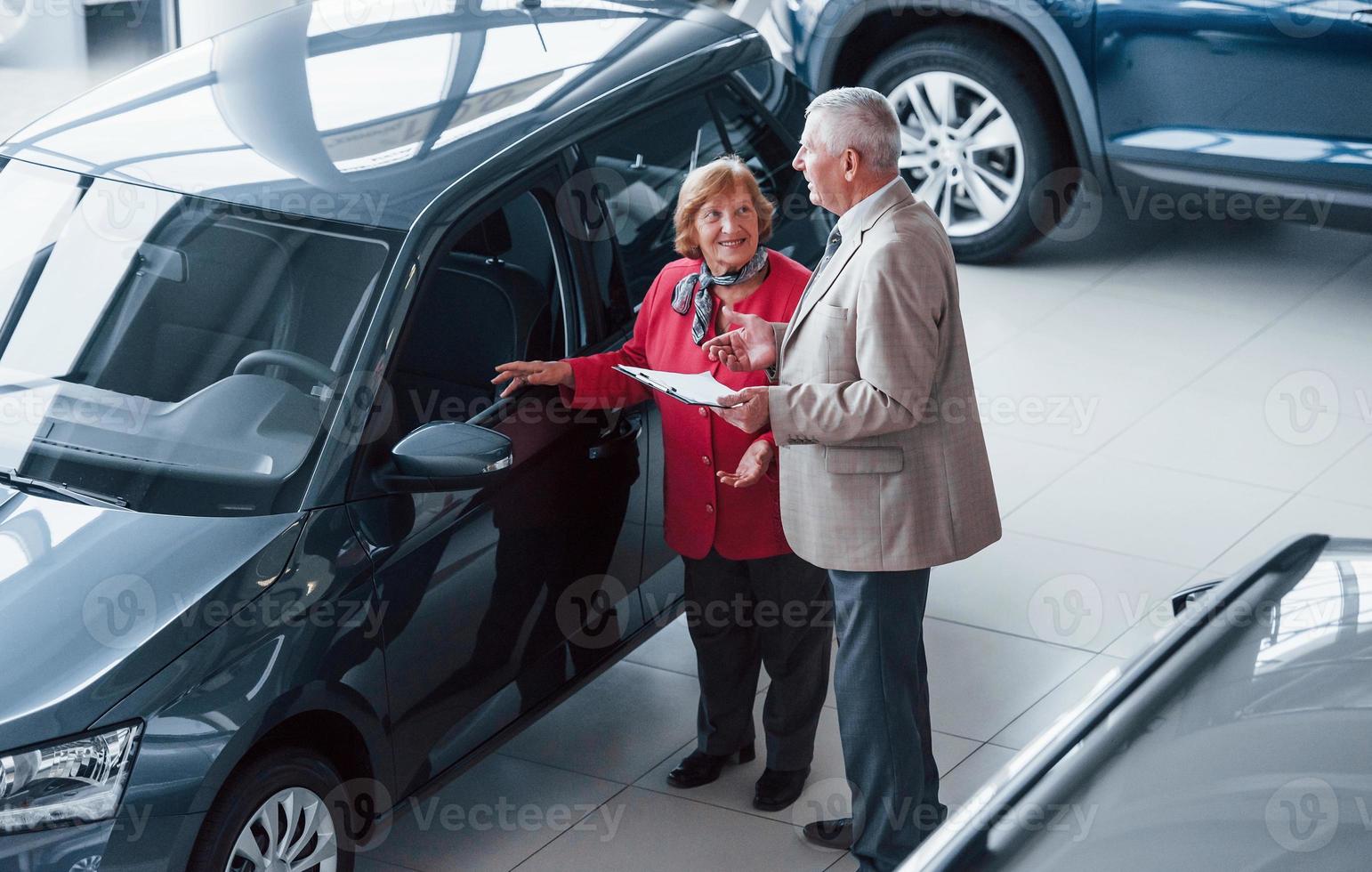vieil homme en tenue de soirée avec bloc-notes soutenant la femme dans le choix de l'automobile photo