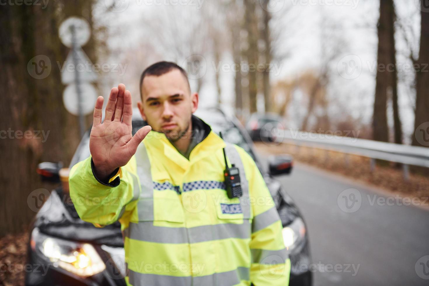 policier en uniforme vert montrant un geste d'arrêt près du véhicule photo