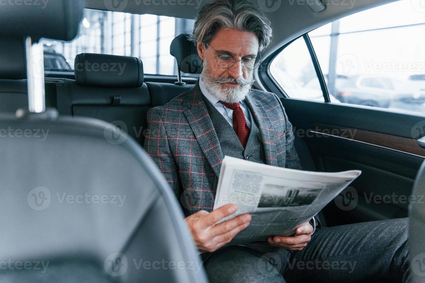 homme âgé moderne et élégant aux cheveux gris et à la moustache lisant le journal à l'intérieur de la voiture photo