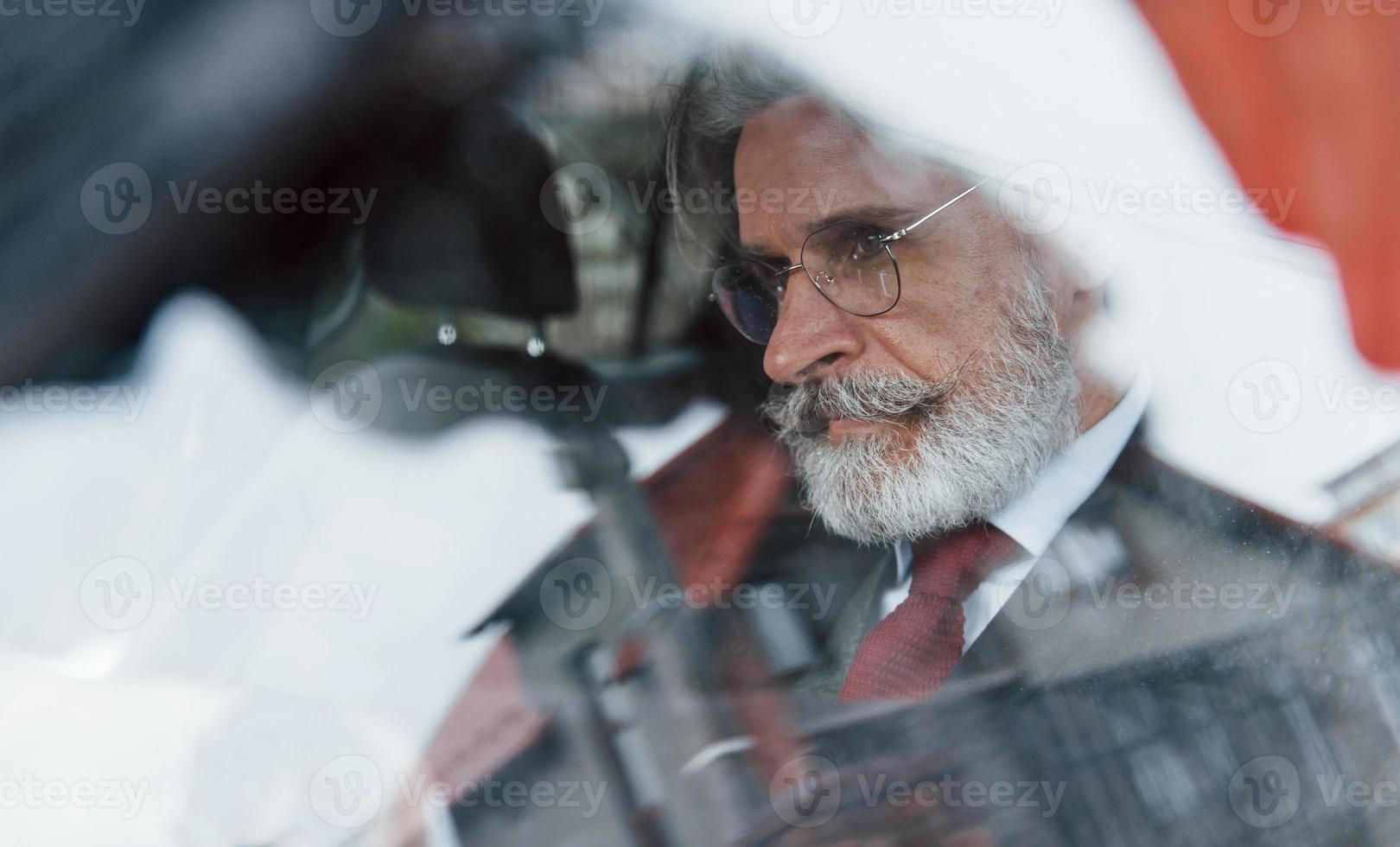 voir à travers la vitre d'un homme senior élégant aux cheveux gris et à la moustache qui se trouve dans la voiture moderne photo