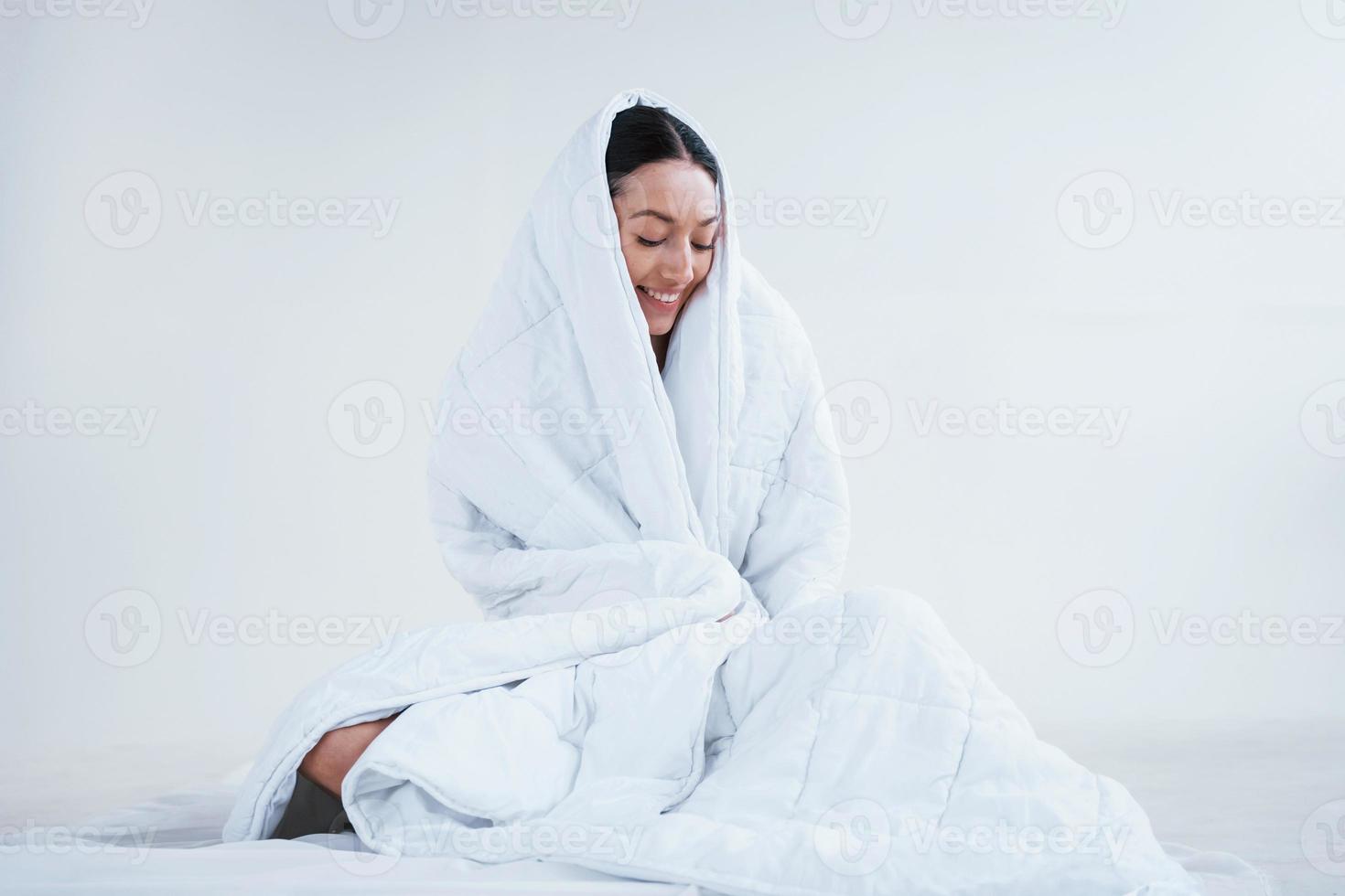 jeune femme couvre le corps avec une serviette et assis dans le studio sur fond blanc photo