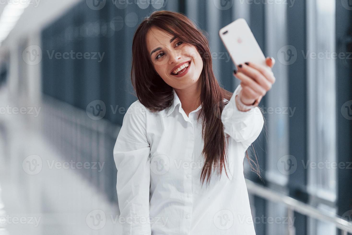 brune en chemise blanche qui marche à l'intérieur dans un aéroport ou un couloir moderne pendant la journée photo