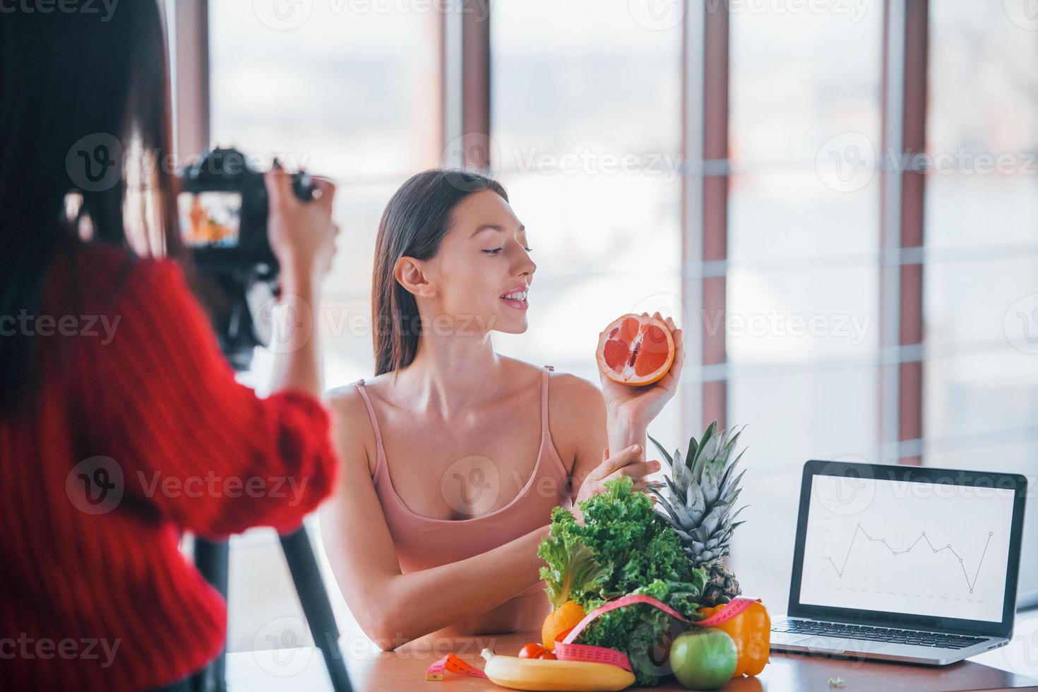 le modèle de fitness a une séance photo par une photographe à l'intérieur près de la table avec des aliments sains