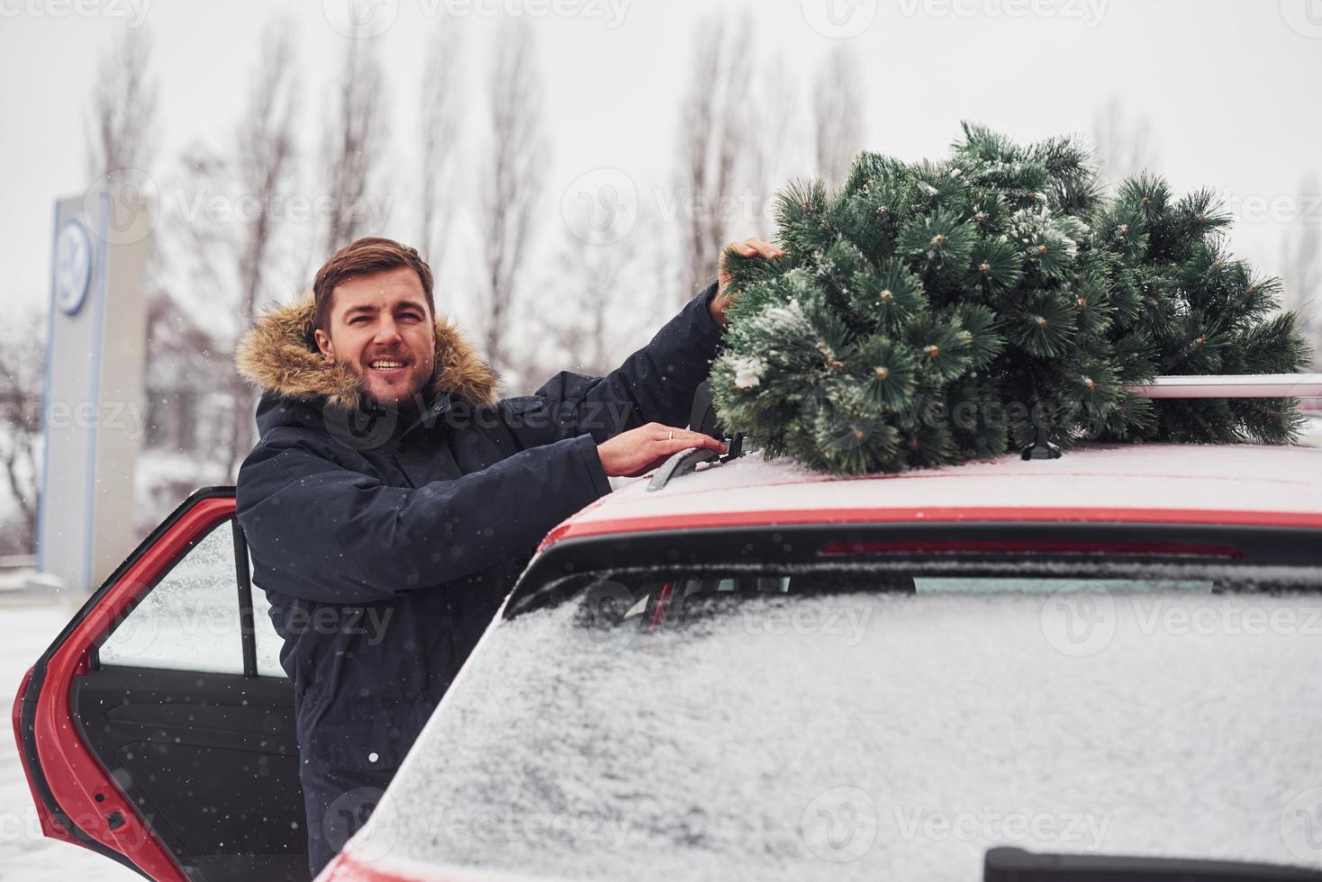 jeune homme debout près de la voiture avec un sapin de Noël vert sur le dessus photo
