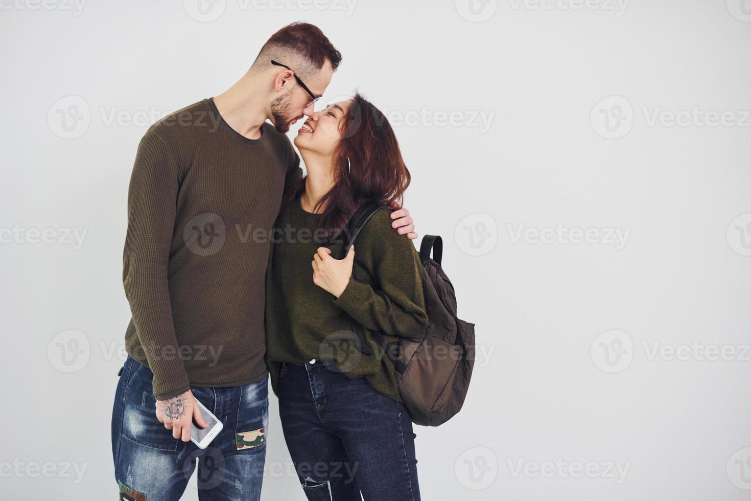 joyeux couple multiethnique avec sac à dos et téléphone debout ensemble à l'intérieur dans le studio sur fond blanc photo