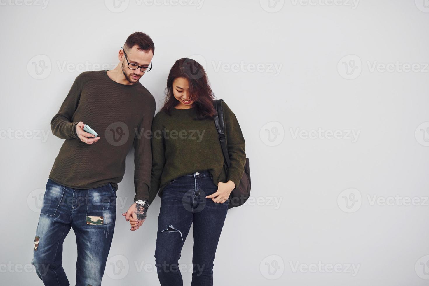 joyeux couple multiethnique avec sac à dos et téléphone debout ensemble à l'intérieur dans le studio sur fond blanc photo